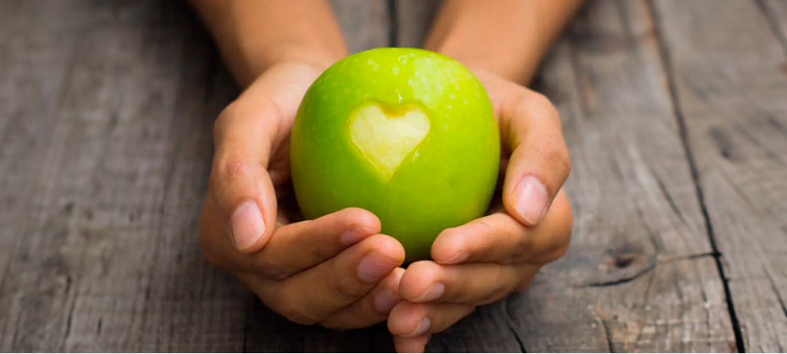 Las manos de una persona sosteniendo una manzana con un corazón dibujado